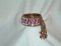 Gold and pink colored metal bracelet for adults.  The bracelet has a "jhumka" (bell) and is inlaid with clear stones.  It has a clasp and can be opened up for easy wearing.  Circumference is 9 inches.