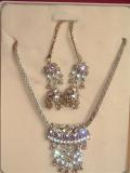 Antique necklace set consisting of a pendant necklace, earrings and ear-chain (worn over the ear lobe) in a dull gold color.  The pendant and earrings are inlaid with purple & clear stones.  The pendant is on a  dull gold-colored metal chain.  Earrings are jhumka-style, and can be worn with or without the "ear-chain".