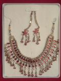 Indian jewelry set consisting of a  necklace / choker, earrings and ear-chain (worn over the ear lobe) in a dull gold color.  The necklace length is adjustable & so can be worn as a choker or necklace.  The necklace is inlaid with teardrop-shaped red stones along its entire length, and so are the earrings.  Earrings can be worn with or without the "ear-chain".